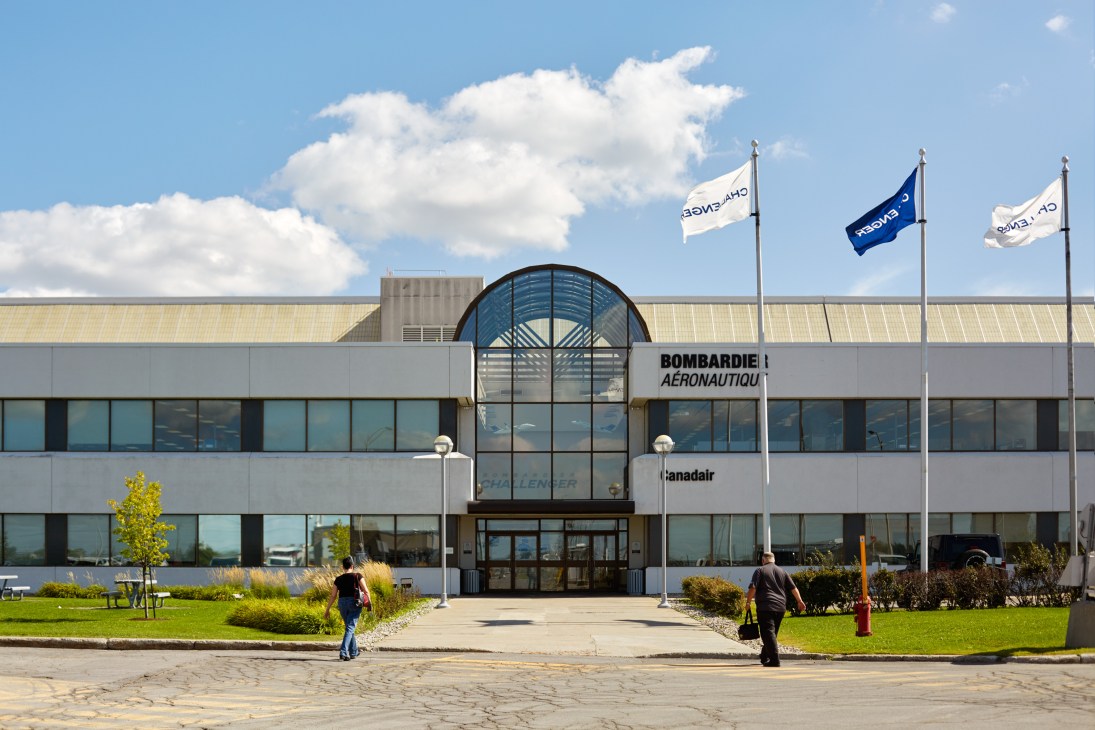 Modern glass and concrete Bombardier Business Aircraft facility with curved entrance and three flagpoles