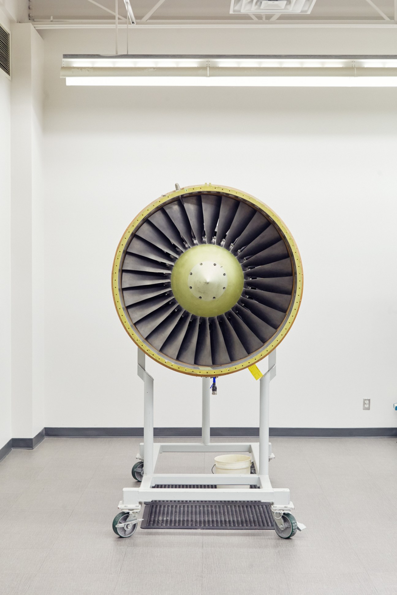 Aircraft jet engine turbine fan mounted on white wheeled stand in clean industrial facility