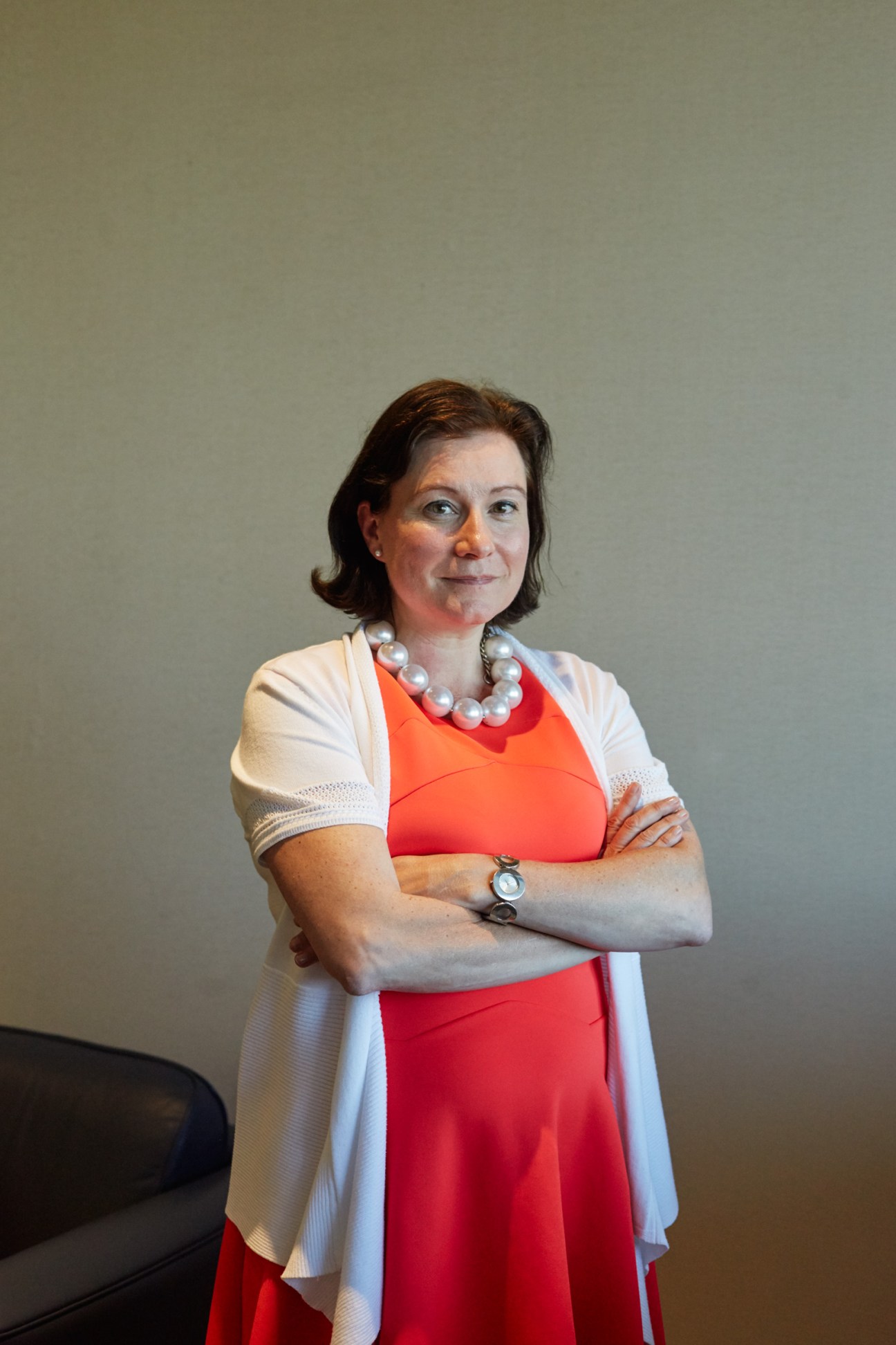 Hélène Gagnon standing with arms crossed in red dress, white cardigan and pearl necklace