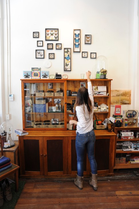 Woman browsing vintage cameras and collectibles displayed in wooden cabinet at The Fox Hunt menswear store.