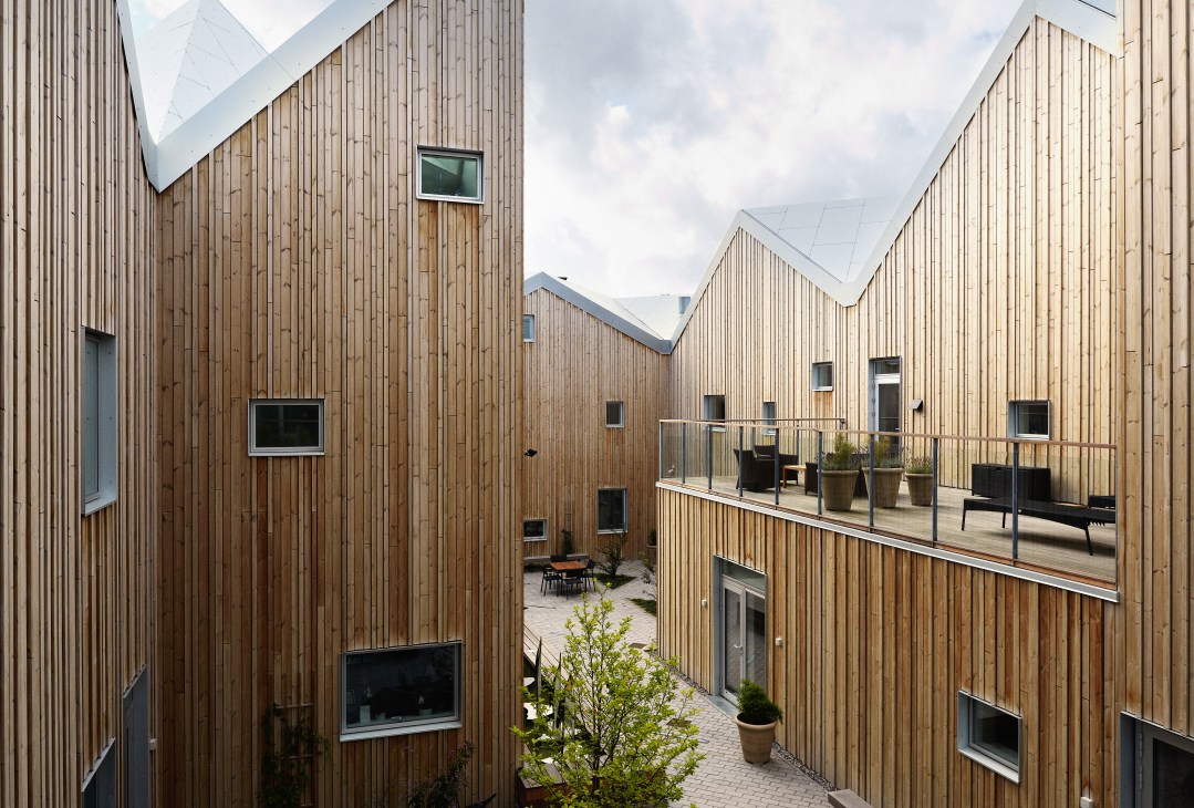 Wood-clad buildings with pitched roofs surrounding a courtyard with greenery and seating areas.