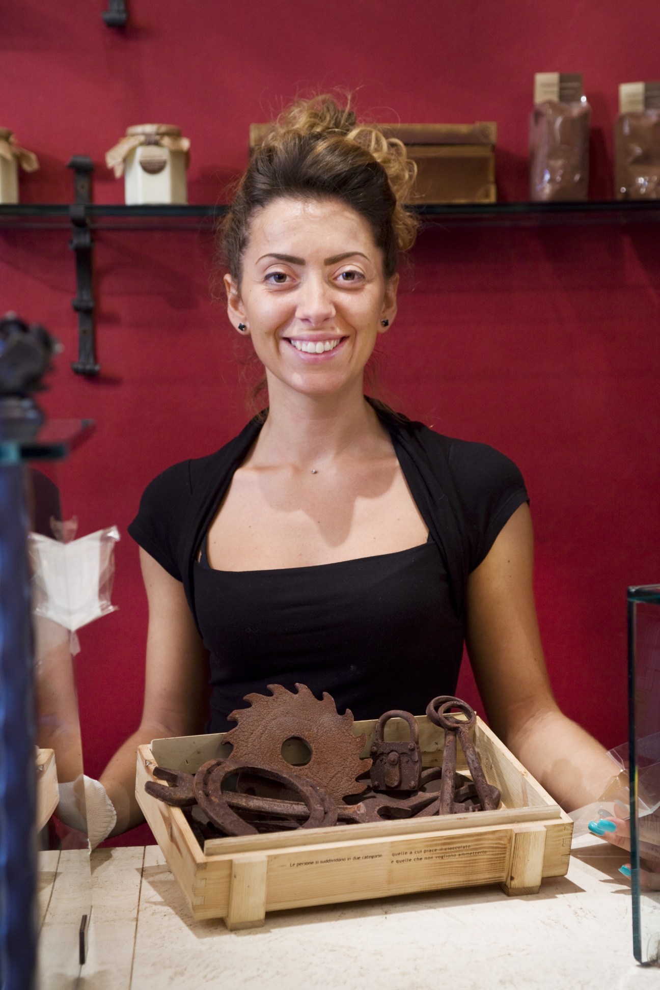 Elisa Fanucci smiles at the camera while holding a wooden box of chocolate items in an artisan shop.