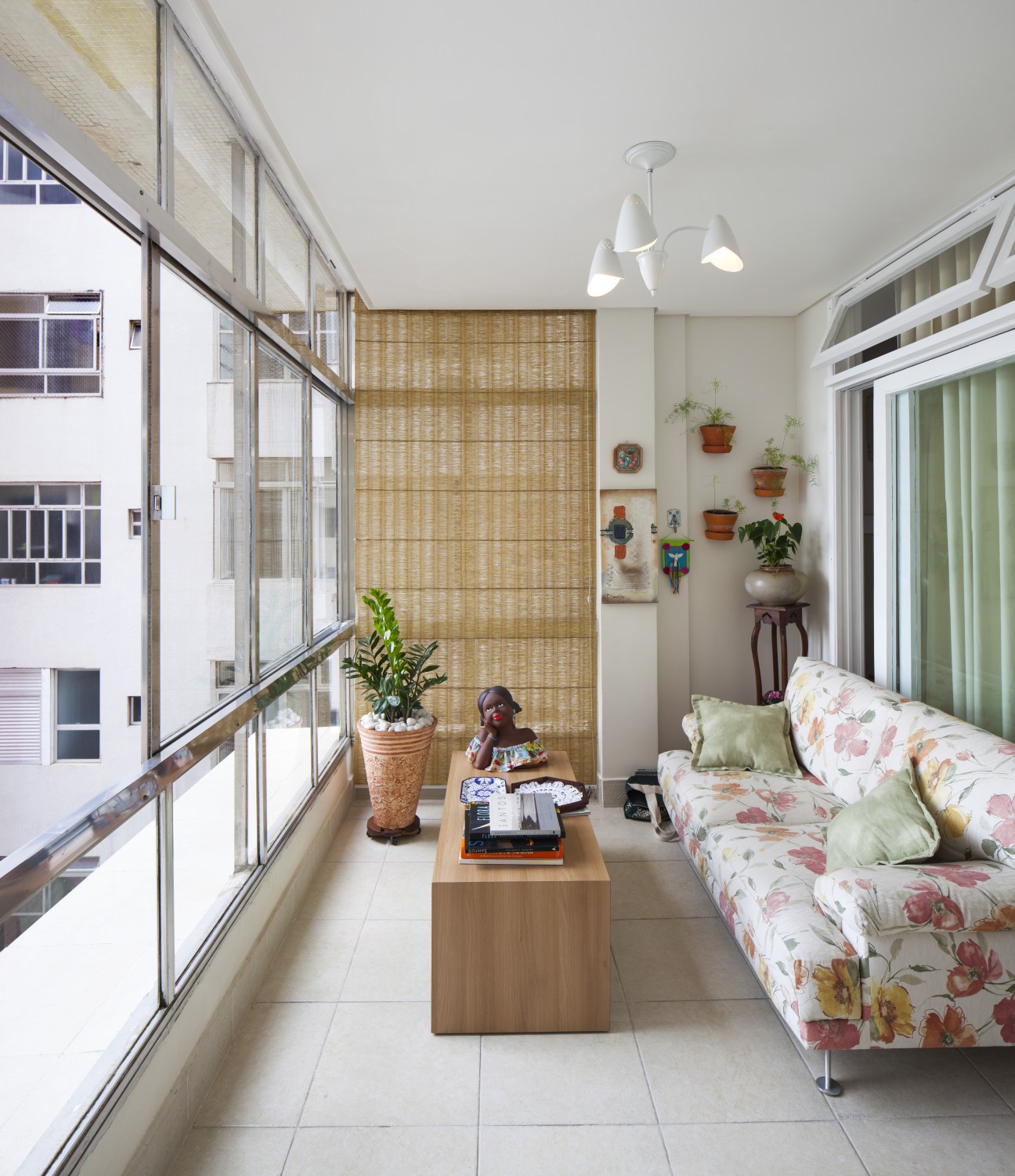 Modern apartment terrace extension with floral sofa, potted plants, and large windows overlooking the building exterior.