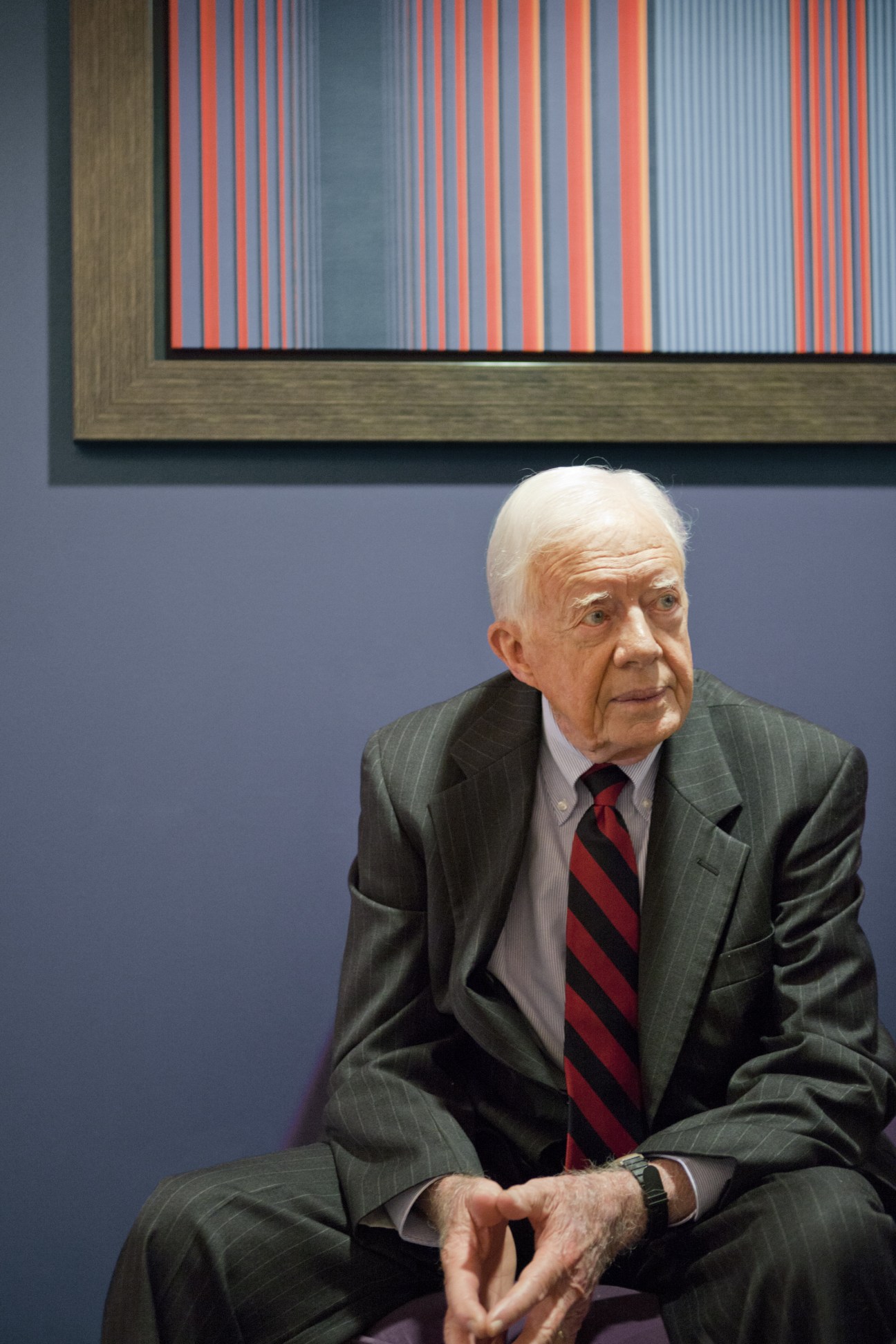 Former US president Jimmy Carter seated indoors wearing a grey pinstriped suit and red tie.
