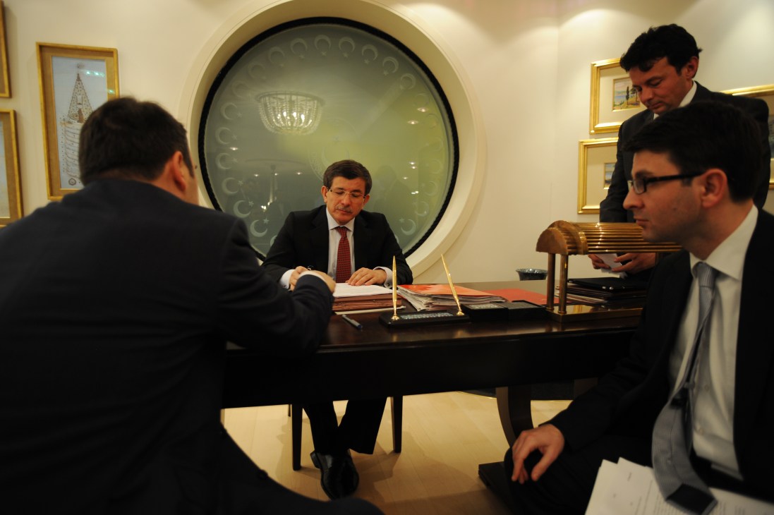 Ahmet Davutoglu meets with aides at a formal desk in an official government office.