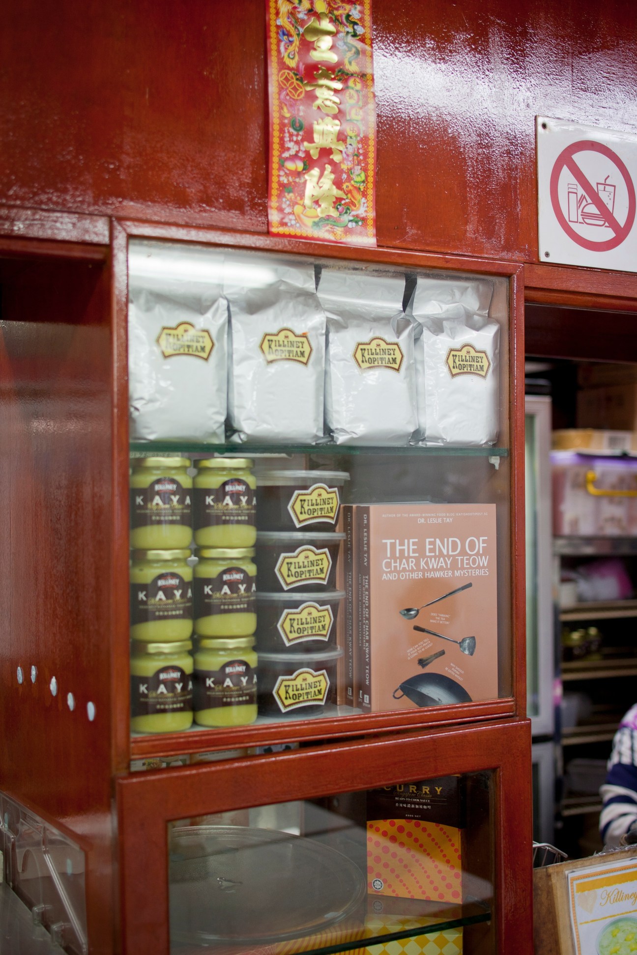 Red wooden display shelf at Killiney Kopitiam with packaged kaya spreads, branded jars and merchandise.