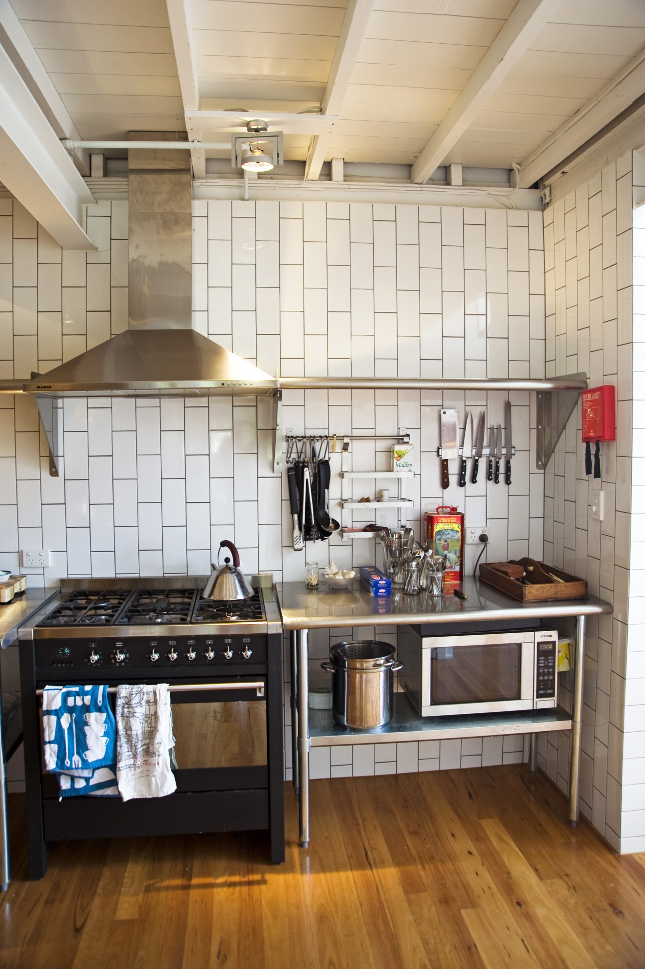 A simple kitchen with white subway tiles, stainless steel appliances, and exposed ceiling beams.
