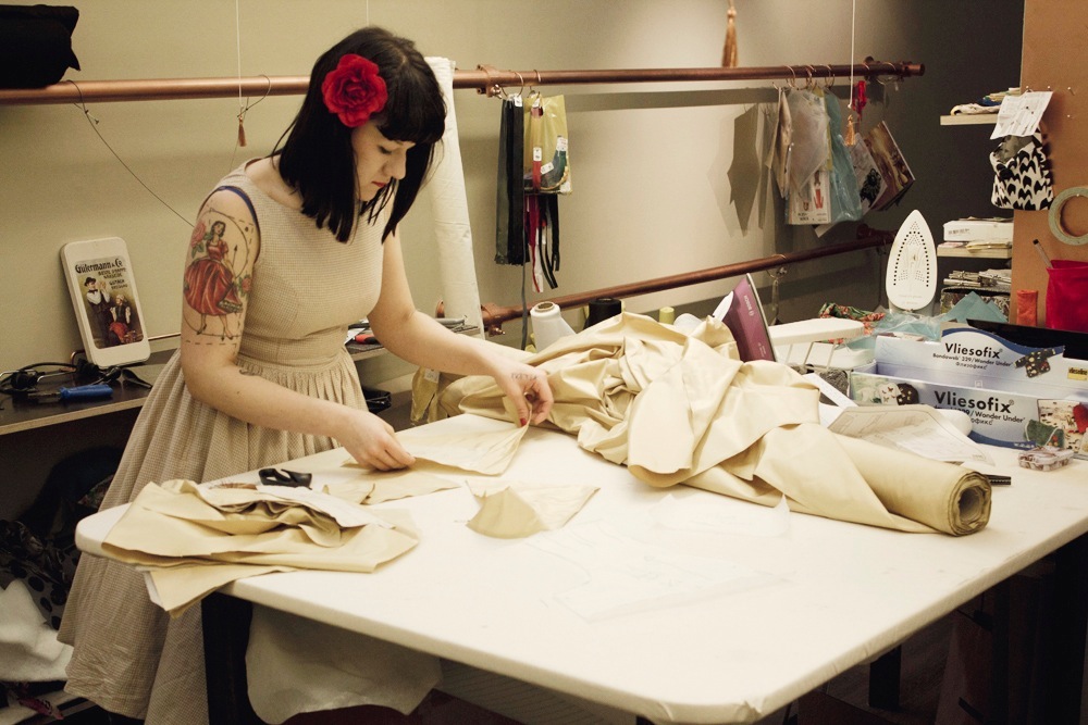 Woman sewing fabric at a cutting table in a Stockholm workshop with sewing machines and materials.