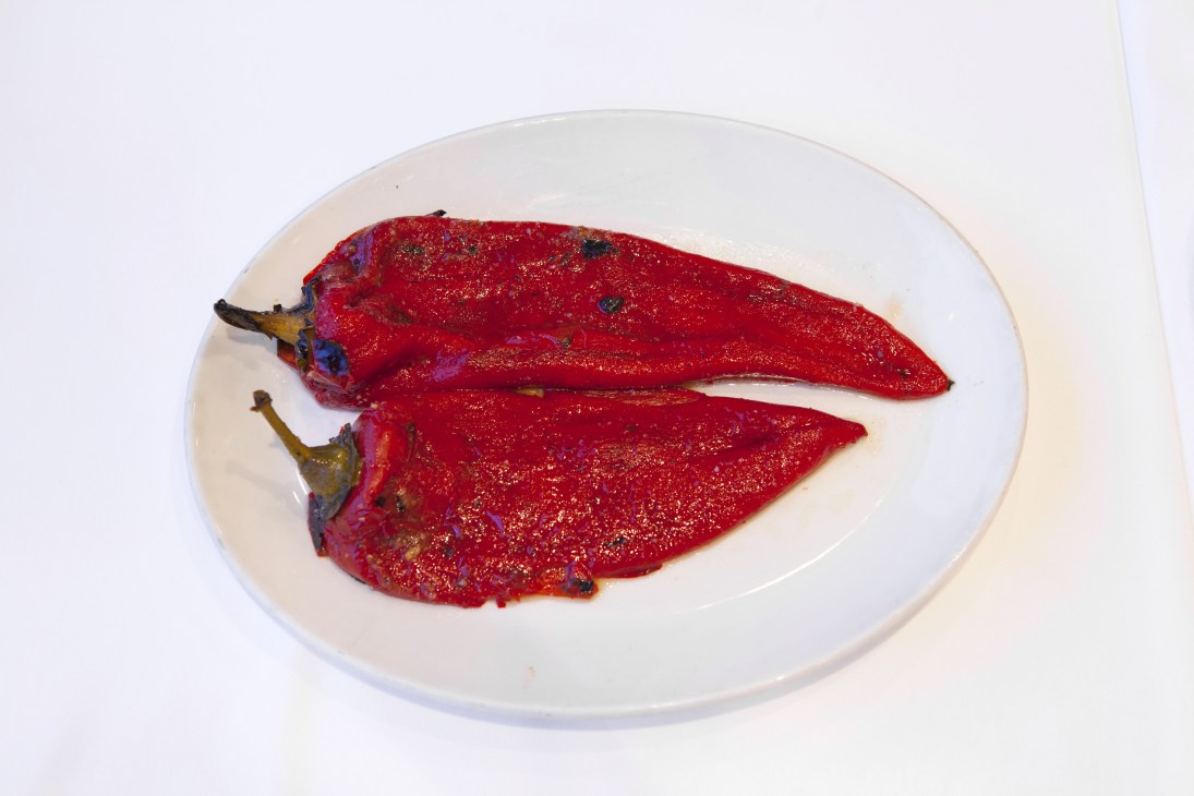 Two roasted red peppers on a white plate against a light background.