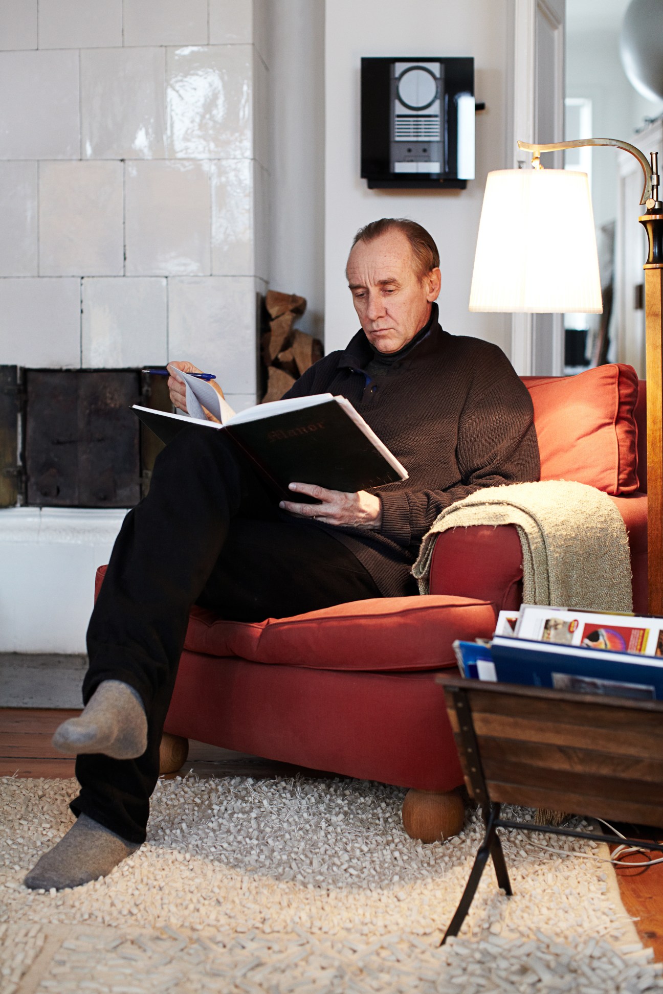 Håkan Nesser, Swedish crime writer, sits reading in a red armchair in a modern interior.