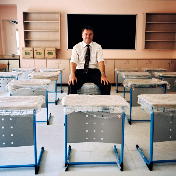 Danny Harrison, principal of the International School Aqaba, sits on a school desk in a classroom.