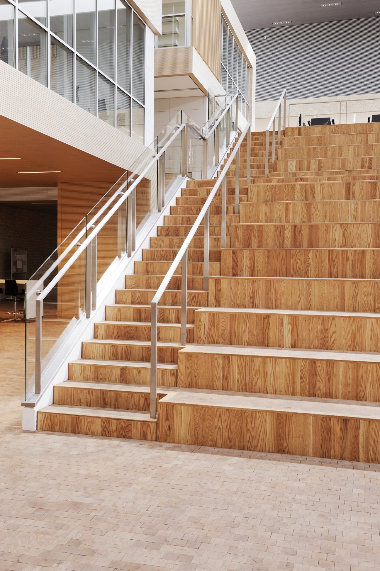 Wooden staircase with white railings in a modern school building with glass walls and natural light.