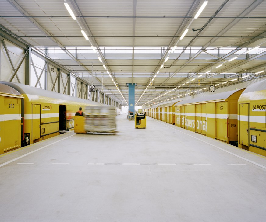 Yellow La Posta containers inside a modern warehouse with fluorescent lighting and a worker operating equipment.