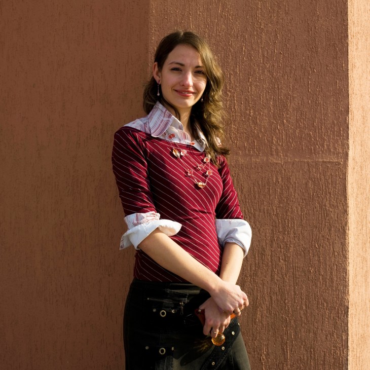 Young woman in red pinstriped blouse smiling against textured brown wall.