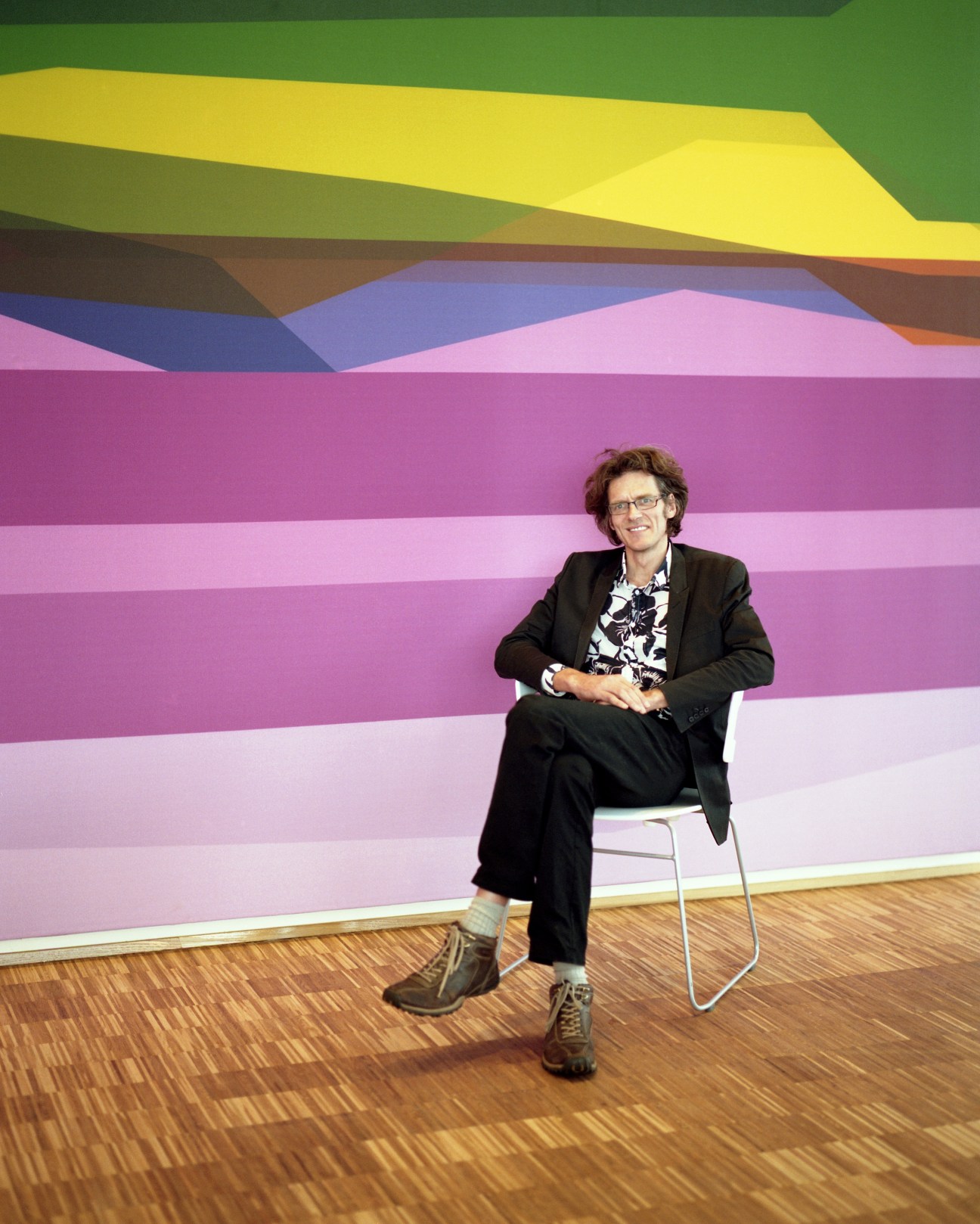 Architect Klavs Hyttel sitting in a modern chair against a colorful striped wall installation.