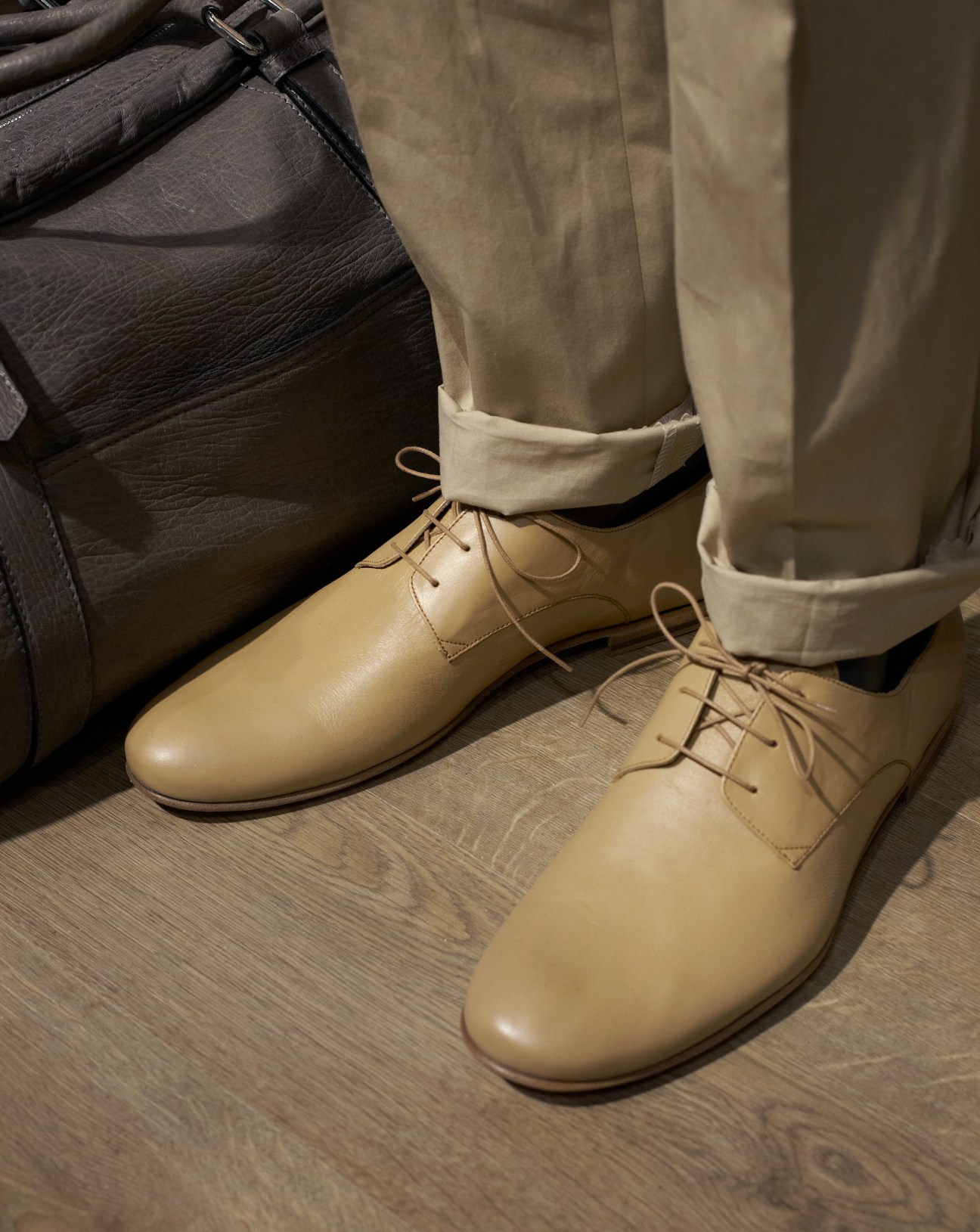 Cream-colored trousers with turn-ups worn with tan leather oxford shoes and a black leather bag.