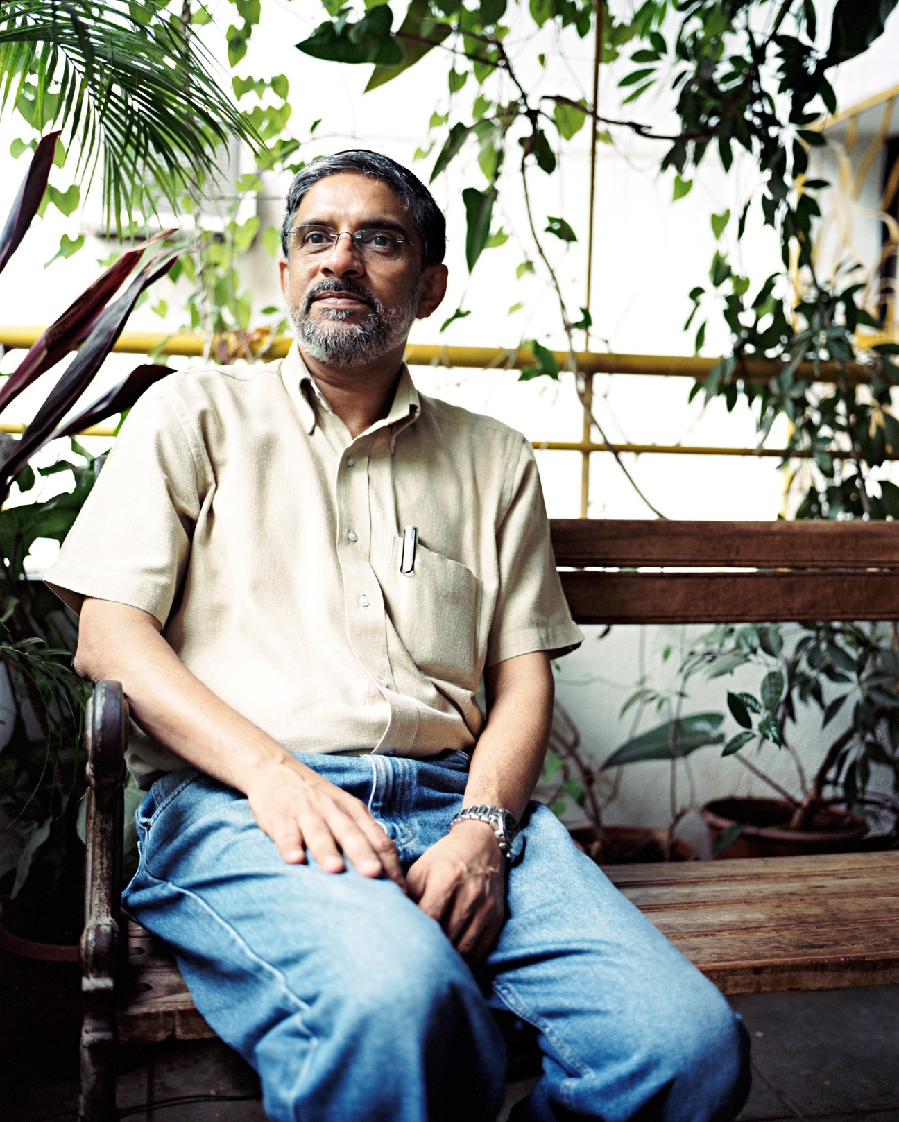 Satish Gokhale, director of Design Directions, sits on a bench surrounded by lush green plants.