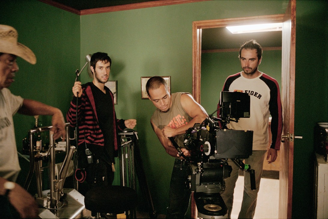 Film crew setting up camera equipment on a green-walled set, with director of photography Andrónico González on the right.