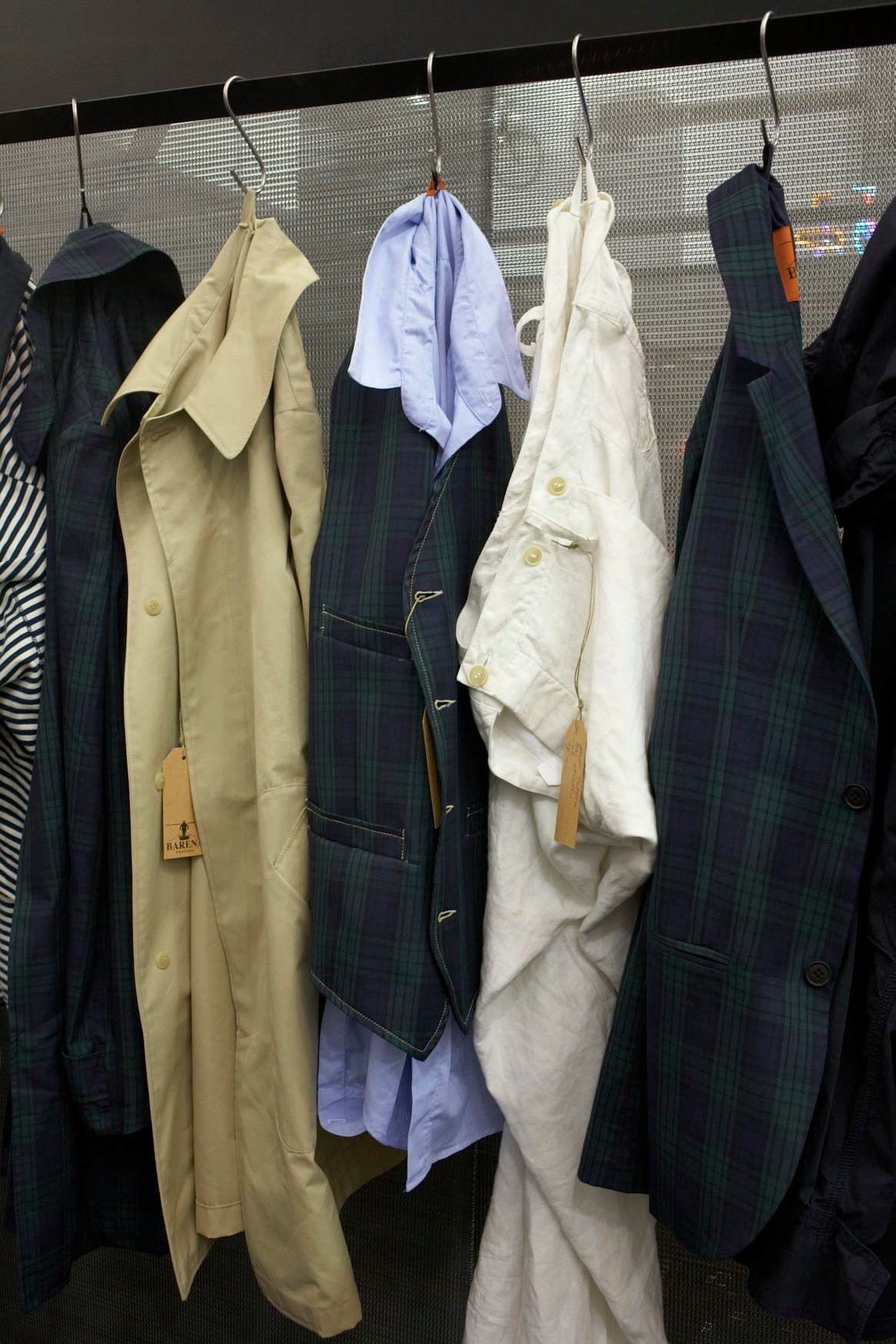 Barena's fishing and hunting-inspired menswear collection displayed on hangers, featuring tailored jackets in navy plaid and cream linen.