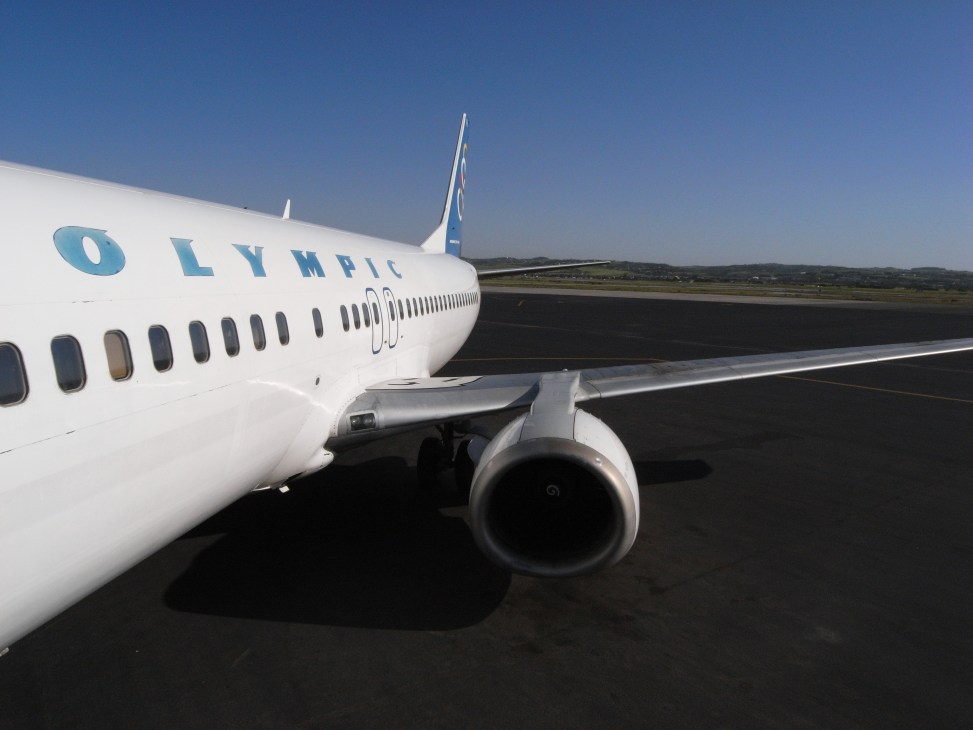 Olympic Airways aircraft parked on runway at Macedonia airport under clear blue sky