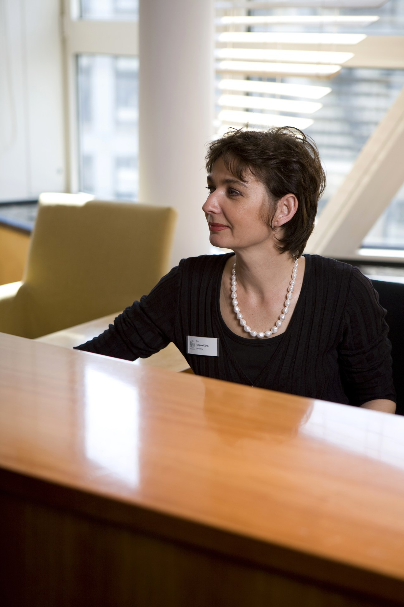 Meoclinic receptionist Tatiana Kühn sits at a desk in a bright, modern office with large windows overlooking Berlin.