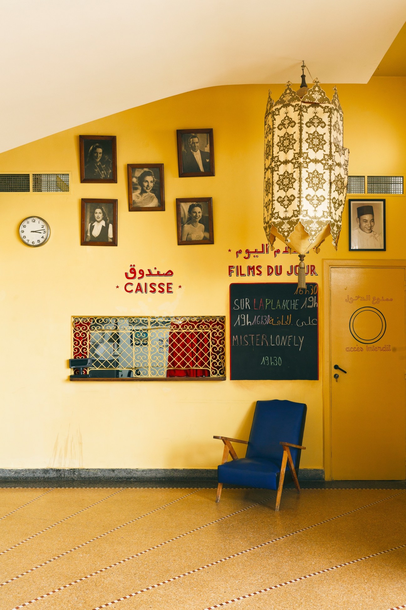 Yellow ticket booth interior at the Cinematheque with framed portraits, vintage lantern, and blue chair.
