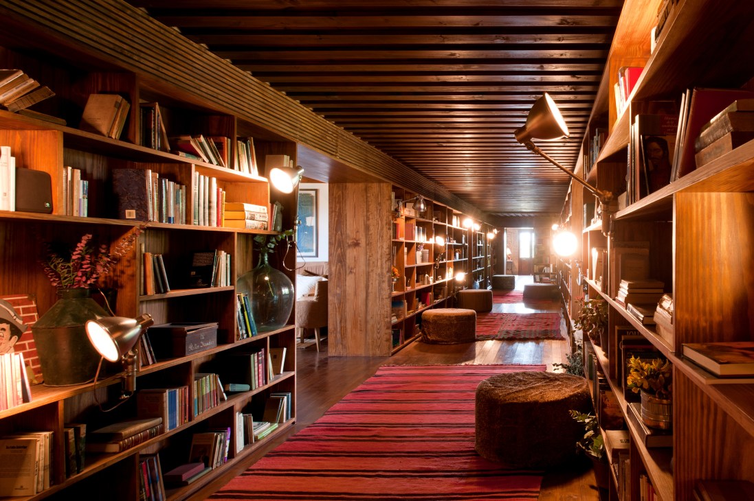 Wood-panelled library corridor with bookshelves, brass pendant lights, and red striped runner rug leading toward the restaurant.