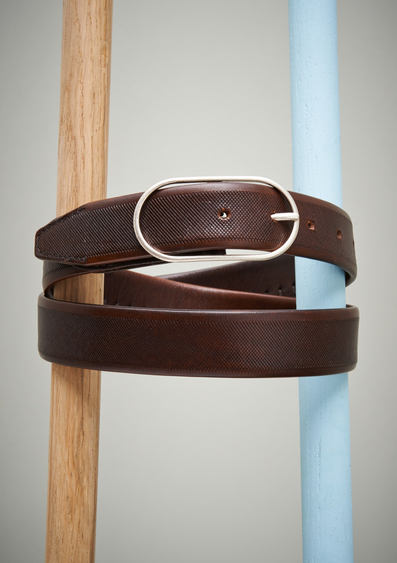 Brown leather belts with silver buckles displayed on wooden and blue poles.