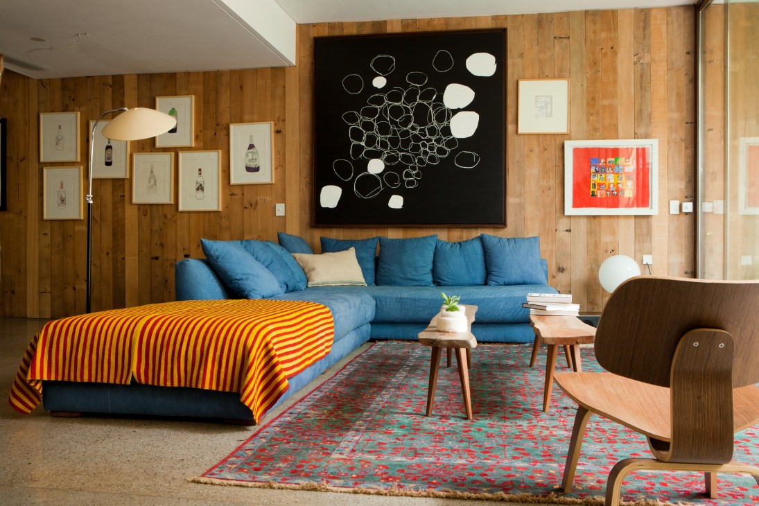 Living room with L-shaped blue sofa, wooden walls, and artwork including a black canvas by Federico Colletta