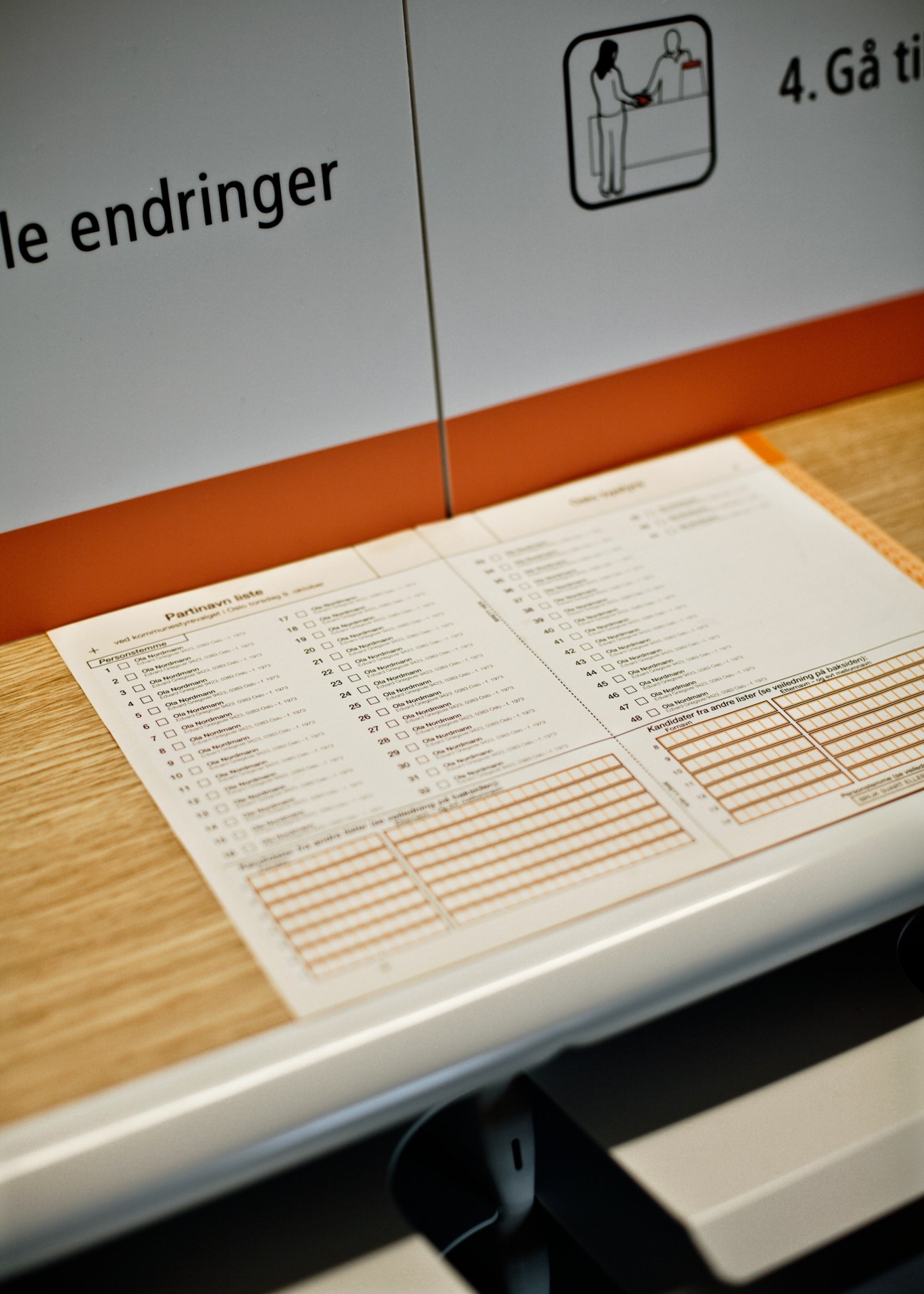 Norwegian ballot paper with orange stripe displayed on oak writing ledge inside voting booth.