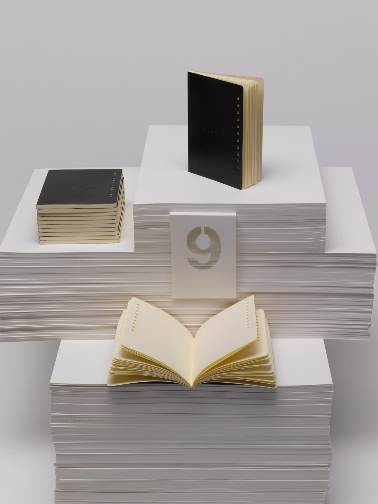 Nava Design stationery set featuring 12 monthly notebooks with punch-holes denoting each month, artfully arranged on stacked paper.