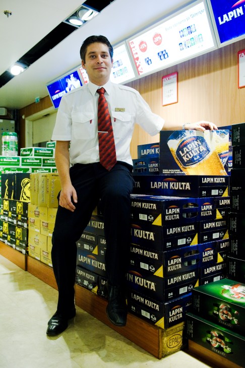 Duty-free shop assistant Kim Lindström standing beside stacked cases of Lapin Kulta beer in the M/S Gabriella's on-board shop.