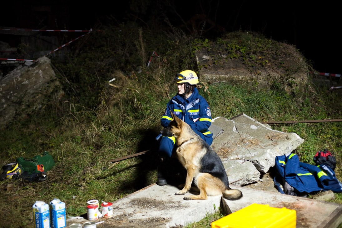 THW volunteer in blue uniform and yellow helmet with rescue dog at disaster training site.