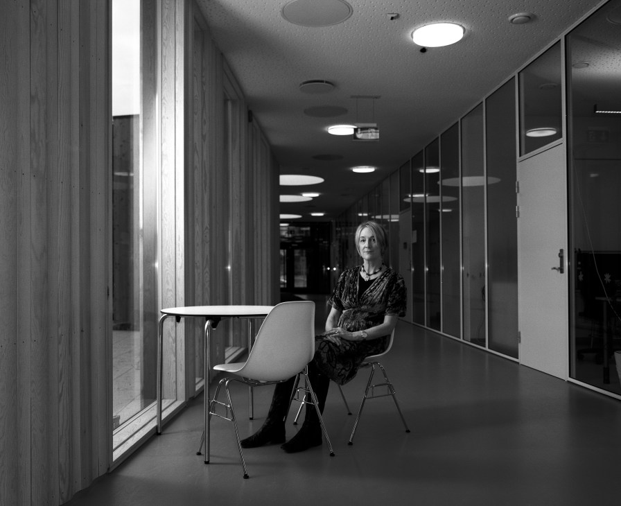 Gail Tennfjord, a Year 2 class teacher, sits at a table in a modern school corridor with wooden panels and recessed lighting.