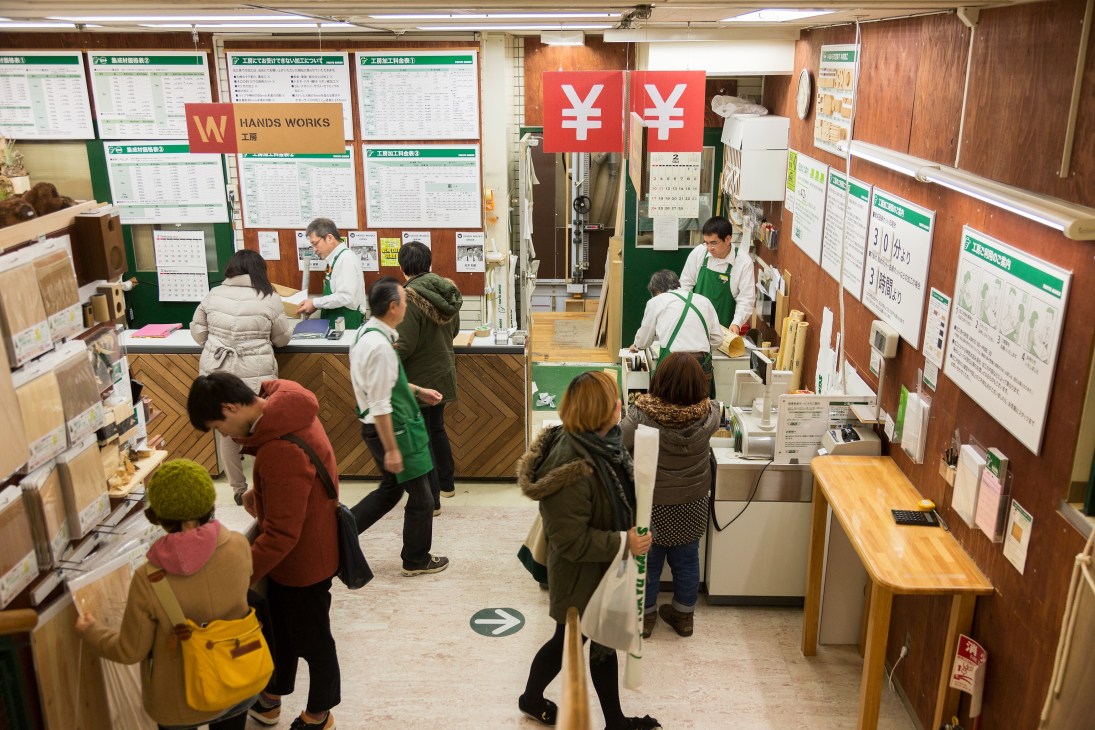 Customers and staff in Tokyu Hands woodwork department with service counter and wooden materials displayed.