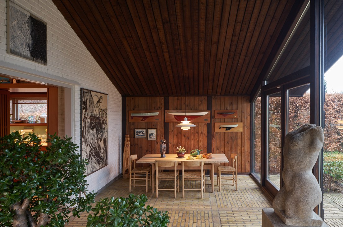 Winter room with wooden panelled walls, dining table, J39 chairs, and large windows overlooking woodland.