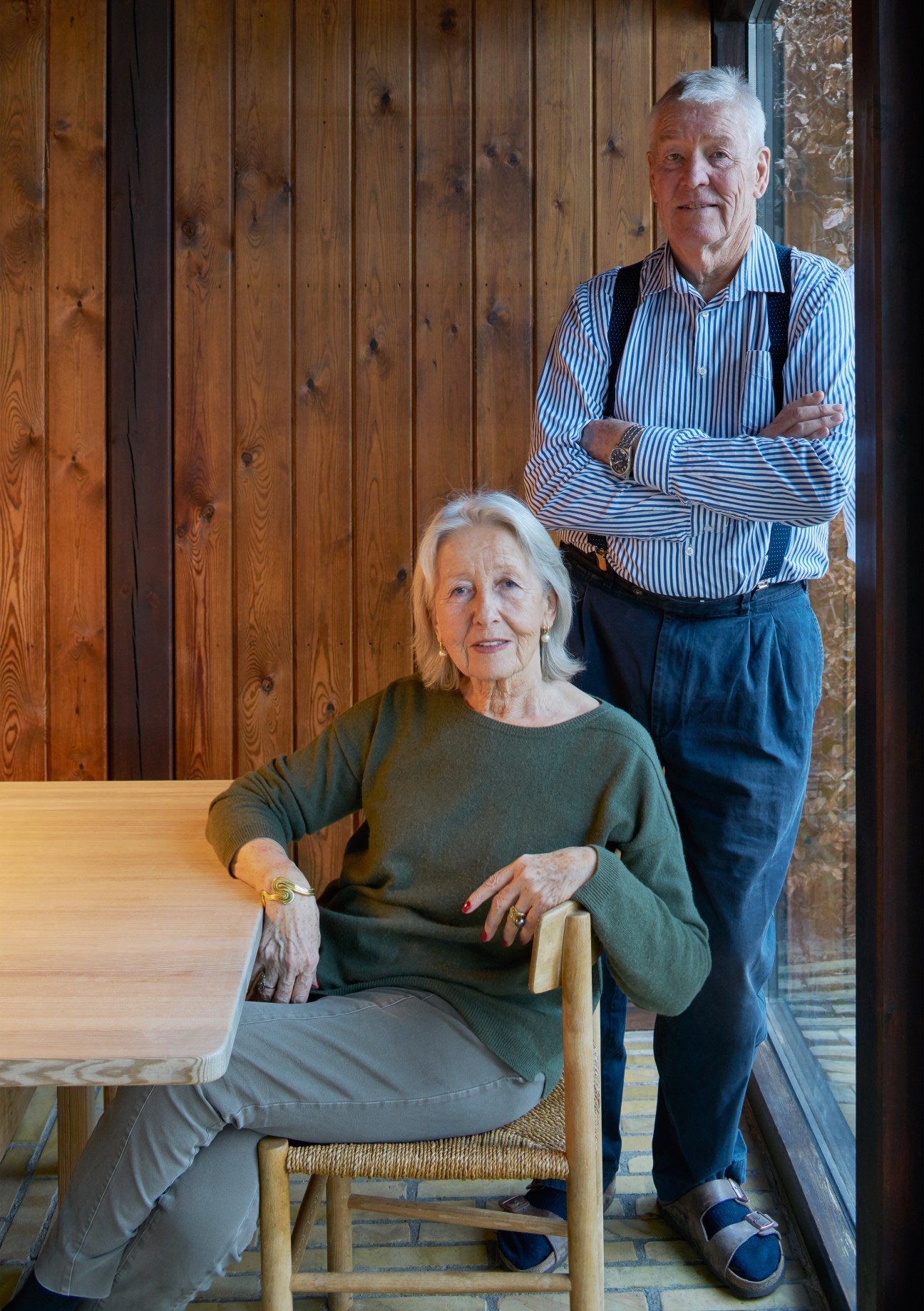 Monika and Ole Paustian sit together in the winter room of their Copenhagen home, with wood-paneled walls visible behind them.