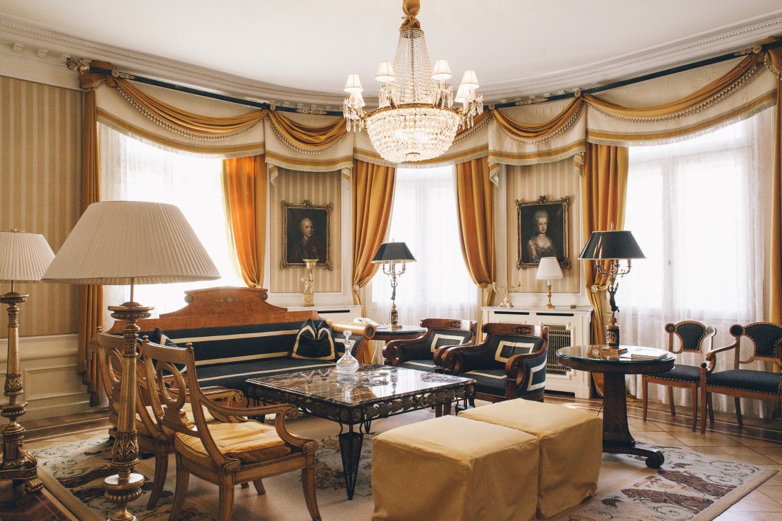 An opulent hotel suite with gold curtains, crystal chandelier, and period furniture reflecting imperial Austro-Hungarian style.