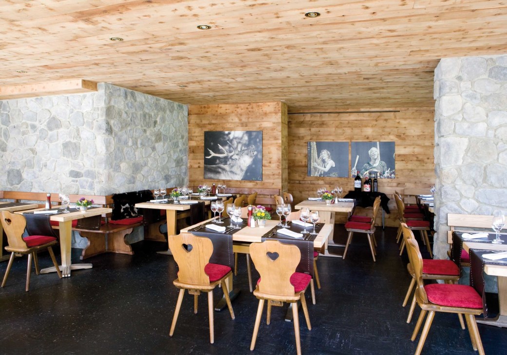 Interior of Lej da Staz restaurant with wooden ceiling, stone walls, wooden chairs with heart cutouts and red cushions.