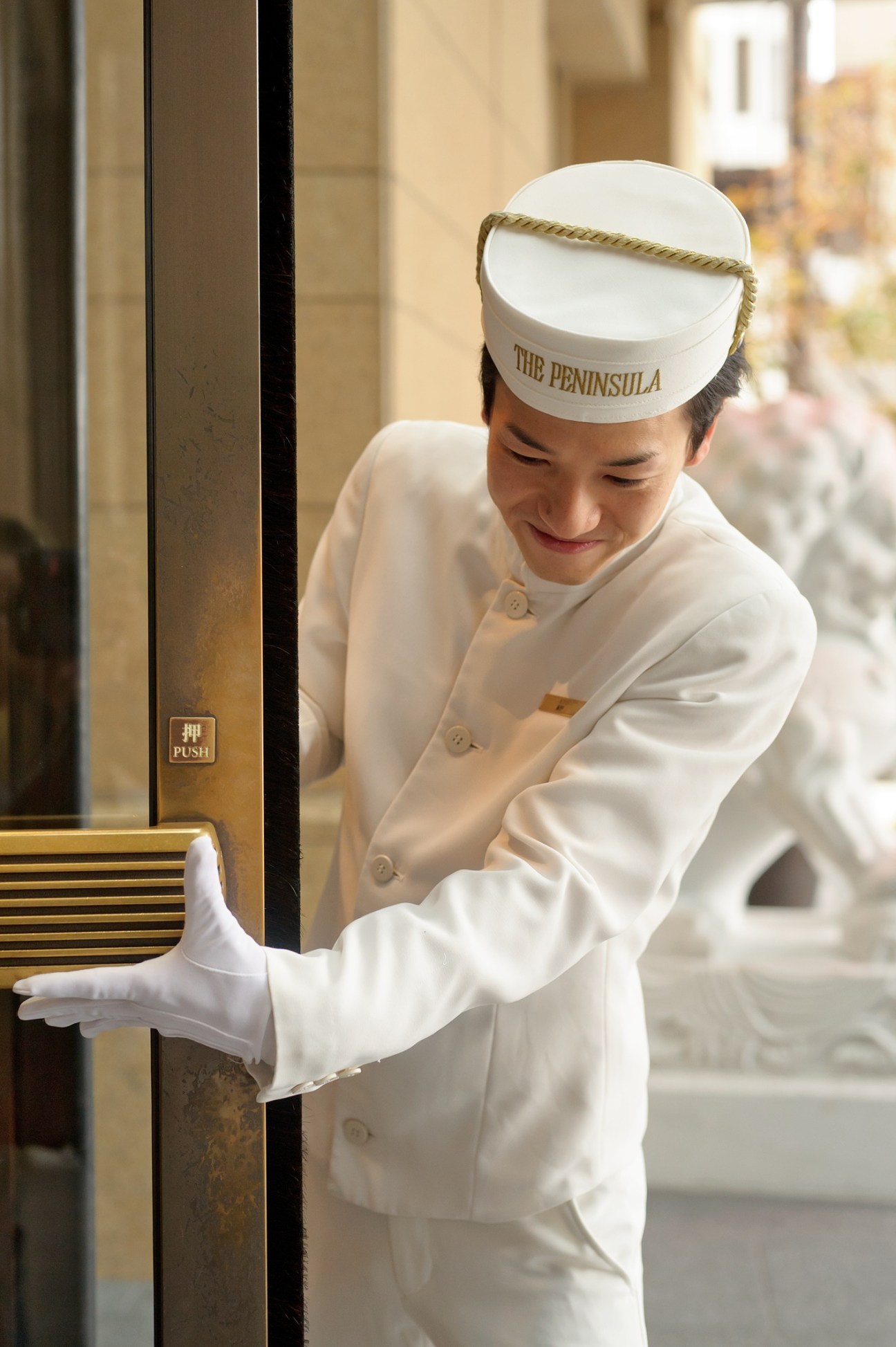 Hotel bellboy in white uniform and cap opening door at The Peninsula Tokyo