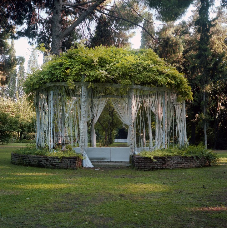 Wedding altar with white curtains and flowering vines in a lush garden setting.