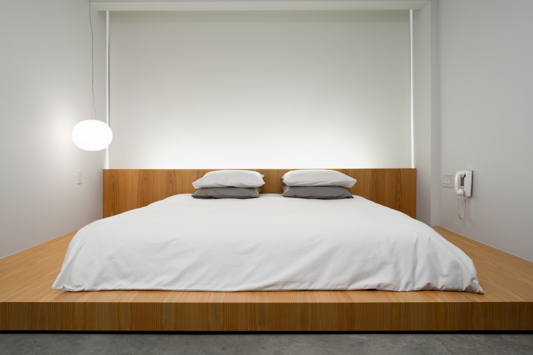 Japanese-style wooden platform bed with white bedding in a minimalist hotel room.