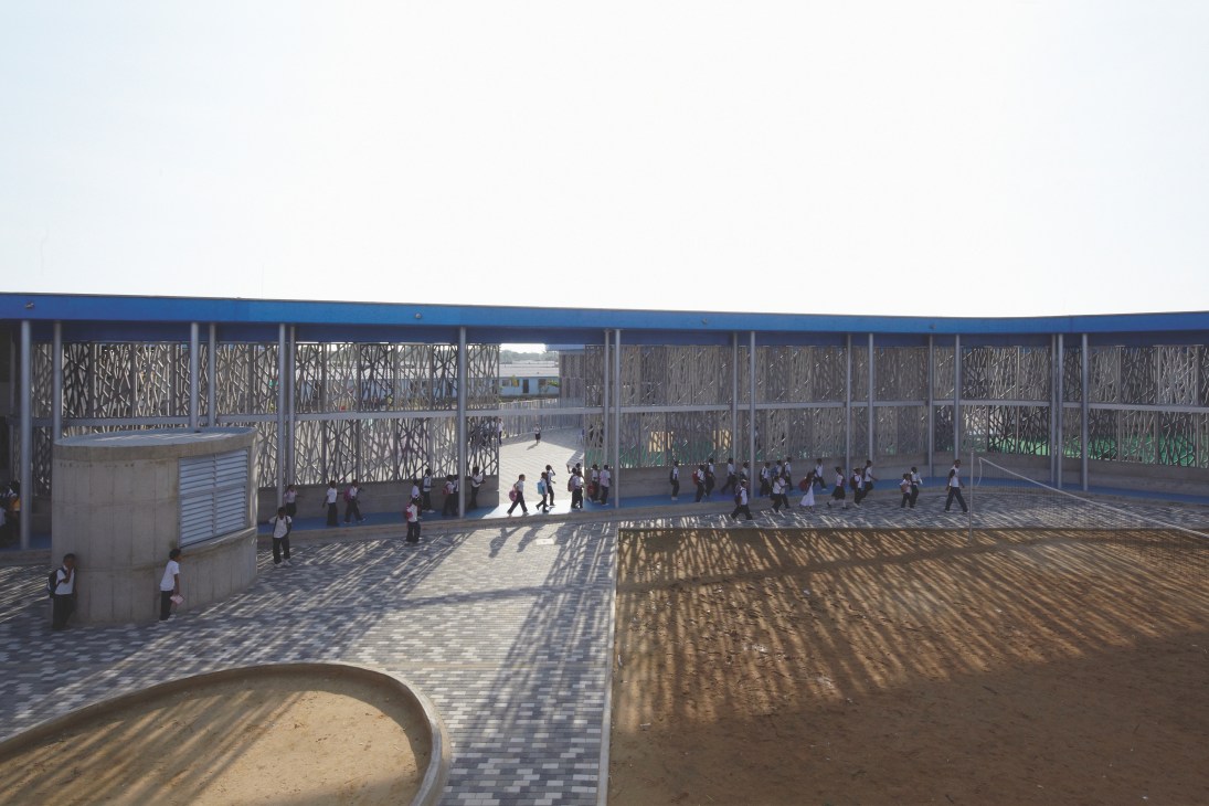Children play in a sunny outdoor playground surrounded by concrete fretwork walls at Flor del Campo school in Cartagena, Colombia.