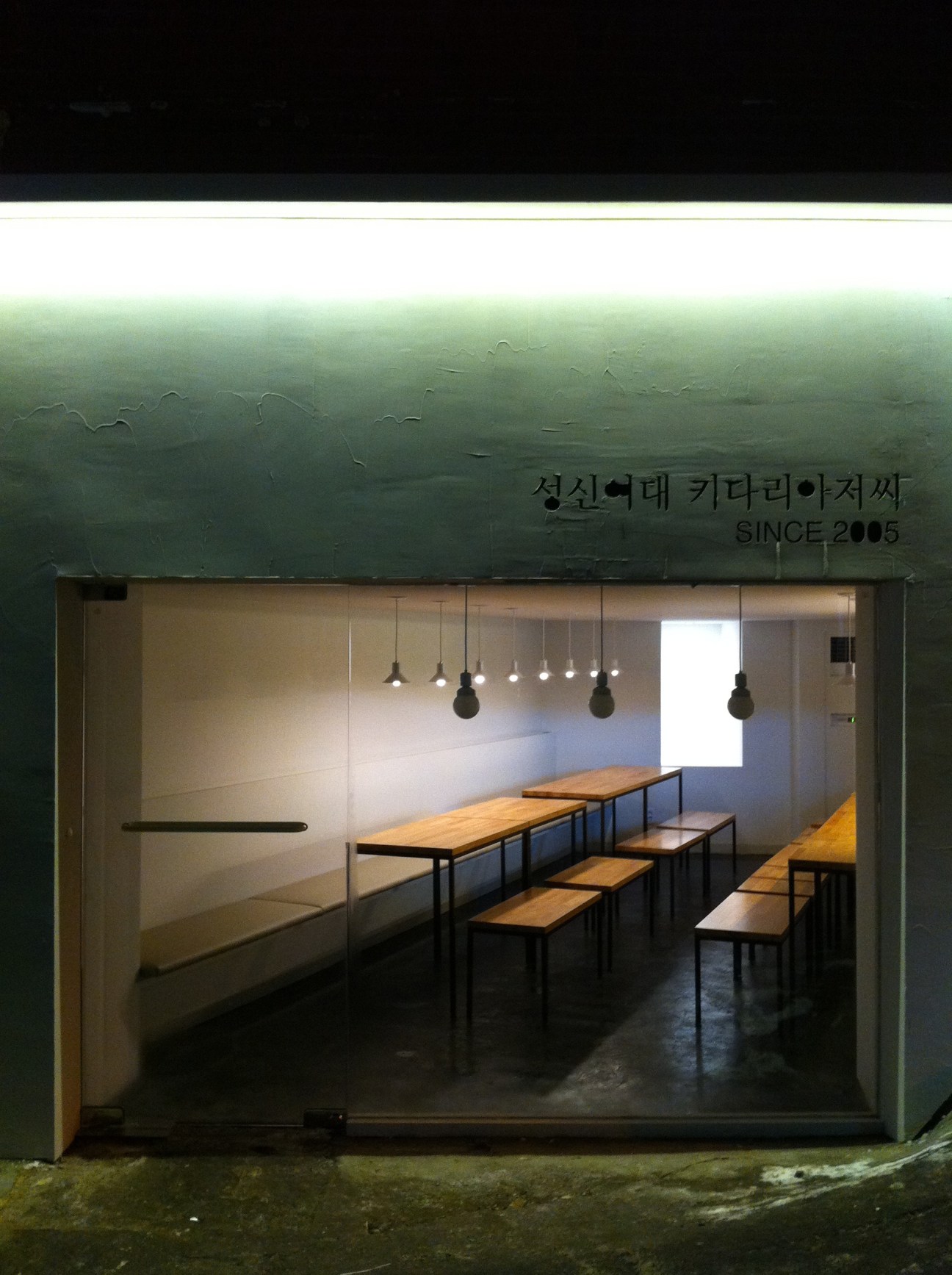 Interior of a minimalist Seoul ramen restaurant with wooden tables, benches, and hanging pendant lights.