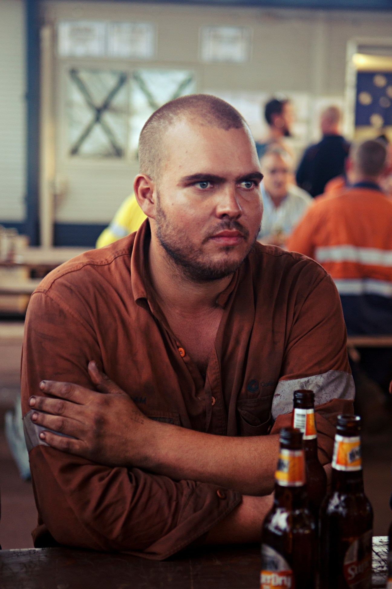 A man in a brown work shirt sits at a table with beer bottles at the Wet Mess pub.