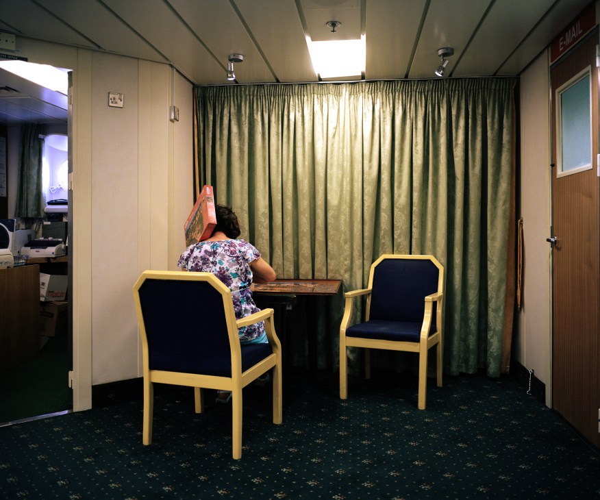 A passenger works on a large jigsaw puzzle at a table aboard the RMS St Helena ship.
