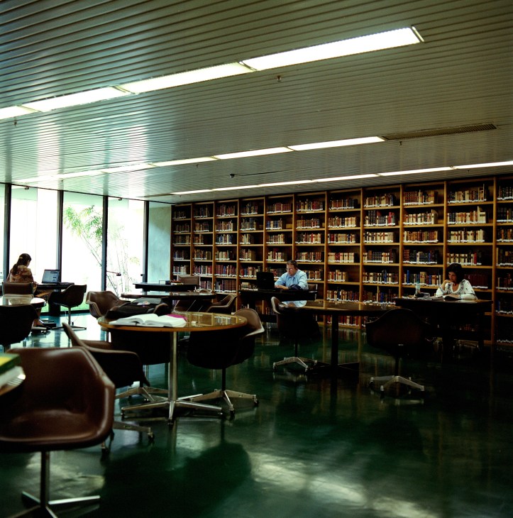 Interior of the Itamaraty Palace library with floor-to-ceiling wooden bookshelves and staff working at desks.