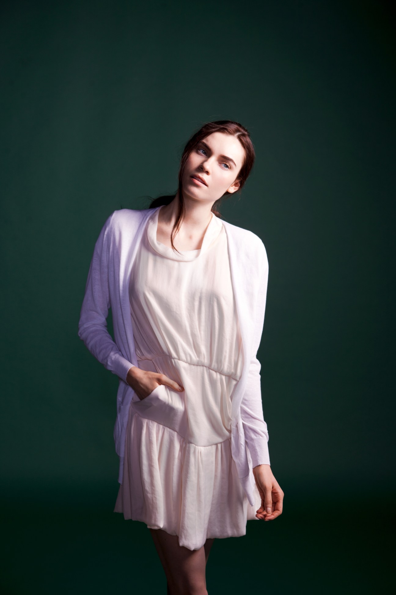 Woman wearing a pale pink draped dress with long sleeves against a green background.