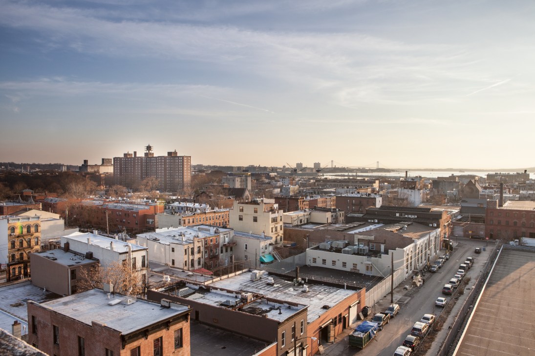 Aerial view of Red Hook, Brooklyn showing residential buildings, rooftops, and waterfront in distance.