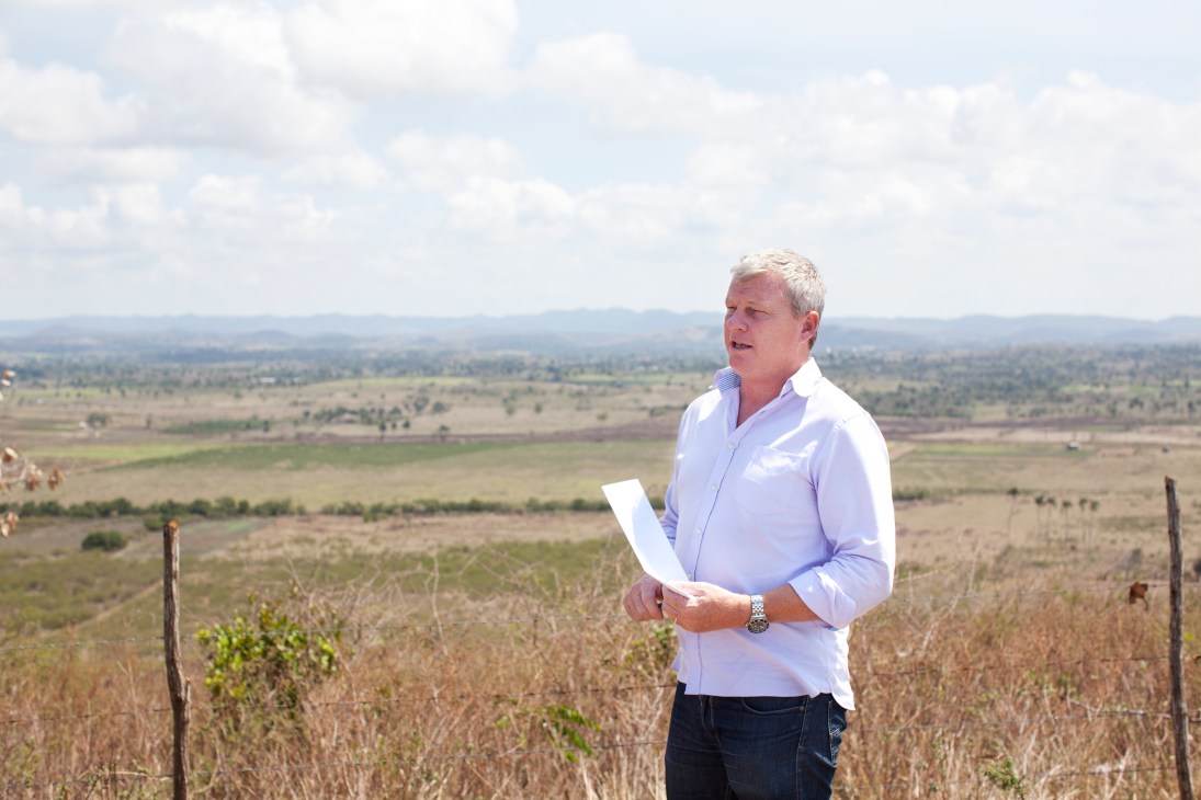 Stephen Purvis stands in an open field holding papers, overlooking Cuban countryside landscape.